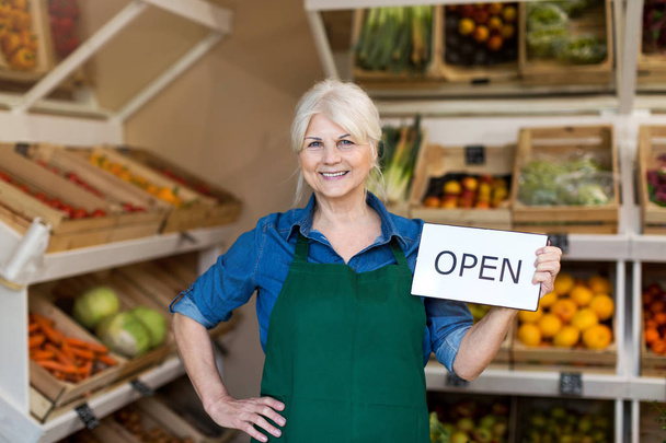 Senior woman holding open sign in organic produce shop - Zdjęcie, obraz