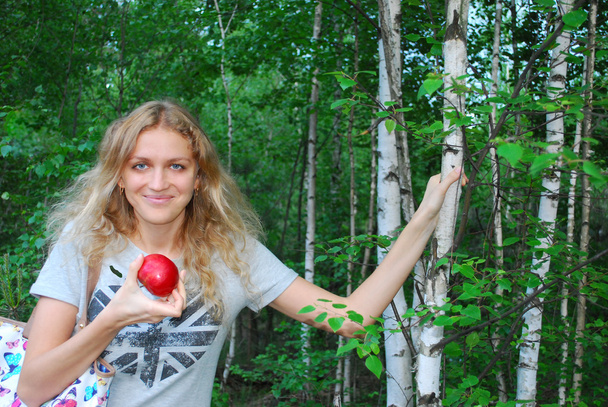 У березовому лісі красива дівчина їсть яблуко
. - Фото, зображення