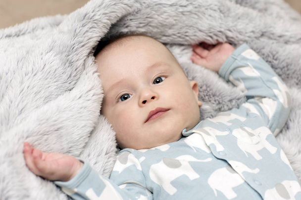 Een baby is op de grijze zachte deken. Een portret van een pasgeborene die in het bed ligt. - Foto, afbeelding