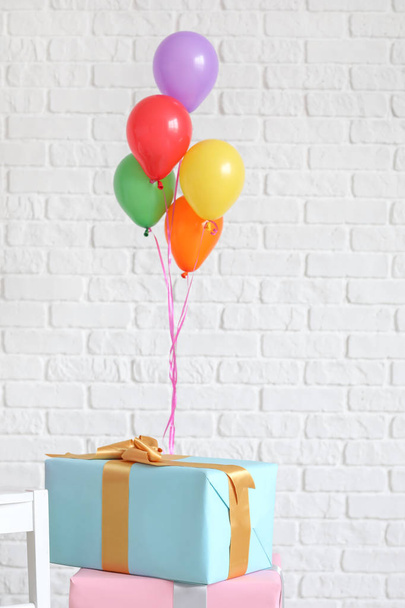 Hermosos regalos con globos de aire cerca de la pared de ladrillo blanco
 - Foto, imagen