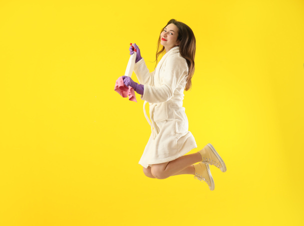 Jumping jeune femme avec des fournitures de nettoyage sur fond de couleur
 - Photo, image