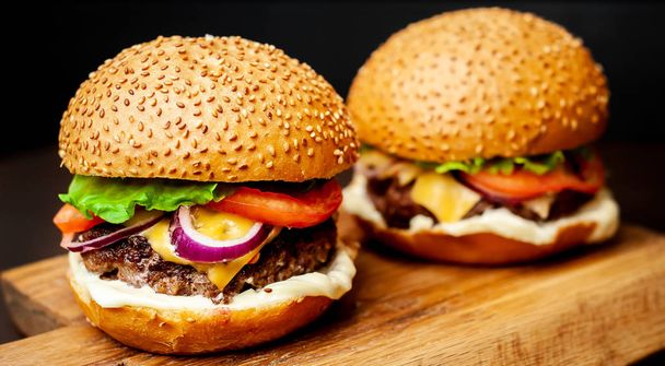 Fresh homemade burgers on wooden chopping board over dark stone background - Foto, imagen