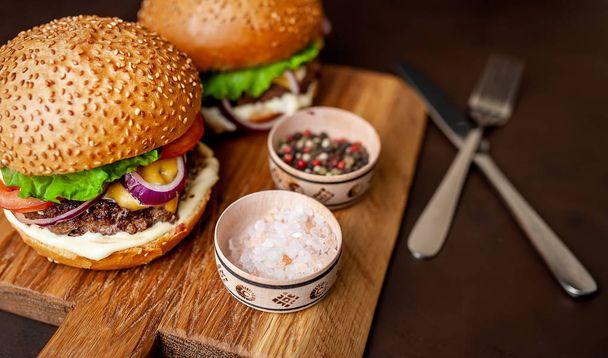 Fresh homemade burgers on wooden chopping board with spices over dark stone background - Foto, Imagen