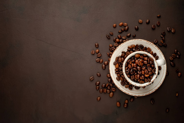 Keramický pohár a talíř plný pražených kávových bobů na pozadí hnědého kamene  - Fotografie, Obrázek