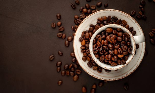 Tasse et soucoupe en céramique pleine de grains de café torréfiés sur fond de pierre brune
  - Photo, image