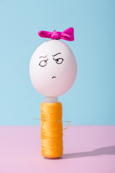 vejce s přídí a hněvivou tváří na závitové cívku na modrém a růžovém - Fotografie, Obrázek