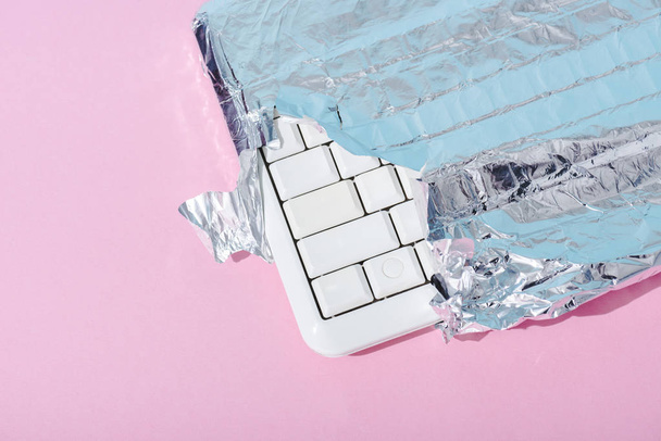 top view of computer keyboard wrapped in silver foil on pink, Chocolate Bar concept - Fotoğraf, Görsel
