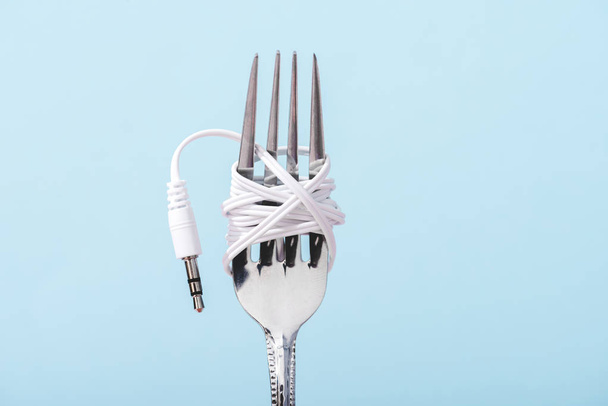 top view of earphones wrapped over metal fork isolated on blue with copy space, music concept - Foto, afbeelding