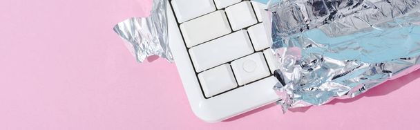 panoramische foto van computer toetsenbord verpakt in zilver folie op roze, chocolade bar concept - Foto, afbeelding