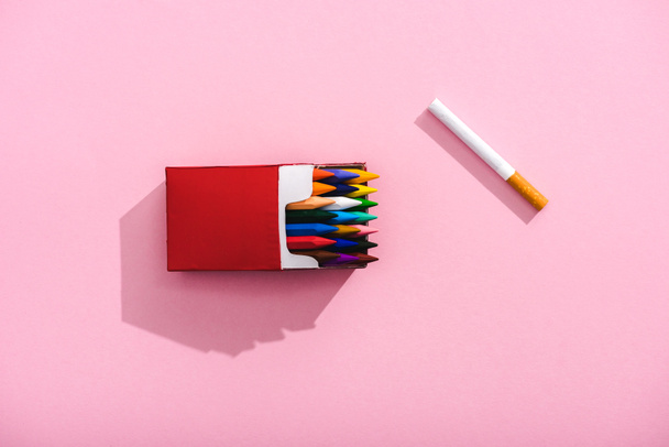 Widok z góry kolorowych kredki w opakowaniu papierosów i papierosa tytoniowego na różowym, koncepcja palenia - Zdjęcie, obraz
