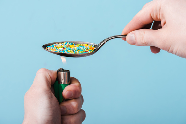 Vista recortada de hombre iluminación cuchara de metal con chispas de colores aislados en azul, concepto de adicción al azúcar
  - Foto, Imagen