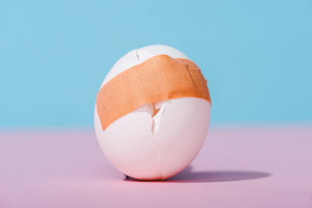 cracked egg with adhesive medical plaster on blue and pink - Foto, immagini