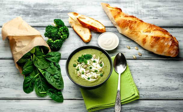 Sopa de crema verde de espinacas y brócoli servida con semillas de calabaza y yogur griego sobre fondo de madera
 - Foto, Imagen