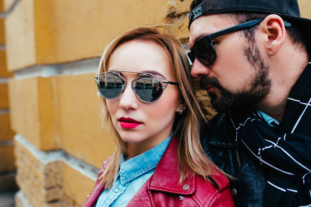 Sexy couple in leather jacket and sunglasses posing over wall in city - Photo, Image