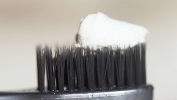 白い歯磨き粉を持つ黒い歯ブラシのための極端なクローズアップは、ベージュの背景に絞られています。メディア。白歯磨きと歯ブラシの黒い剛毛、デンタルケアの概念. - 写真・画像
