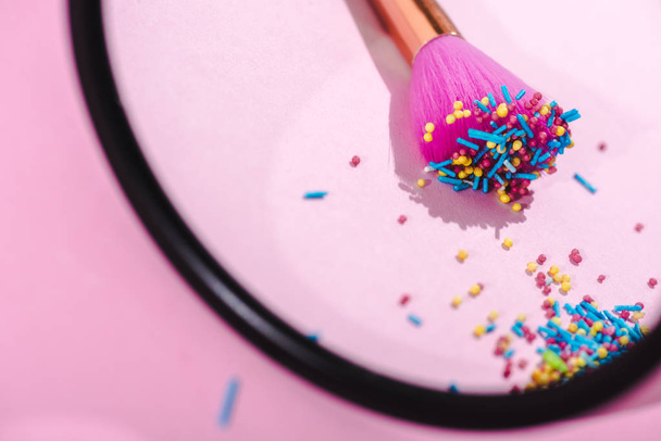 selective focus of makeup brush covered in colorful sprinkles reflecting in mirror on pink - Fotoğraf, Görsel