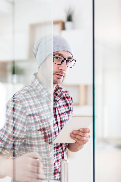 Portrait of fashionable architect or designer with tablet device opening glass office door. - 写真・画像