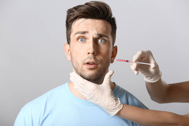 Scared man and hand holding syringe for anti-aging injection on light background - Photo, Image