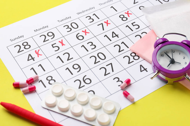 Εμμηνορροϊκό ημερολόγιο με χάπια και ξυπνητήρι στο φόντο του χρώματος - Φωτογραφία, εικόνα