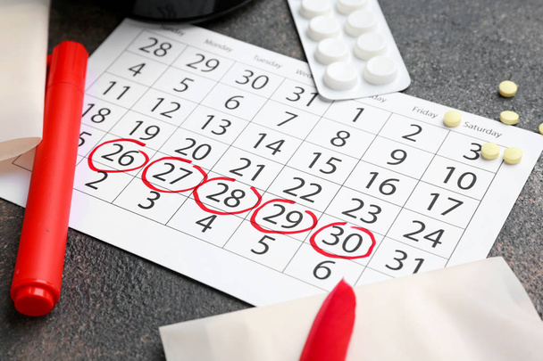 Calendario mestruale con prodotti femminili e pillole su sfondo grigio
 - Foto, immagini