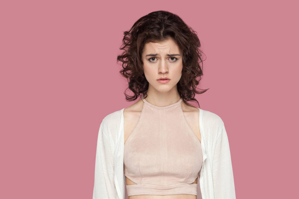 sad beautiful brunette young woman with curly hairstyle in casual style standing and looking at camera on pink background. - Фото, зображення