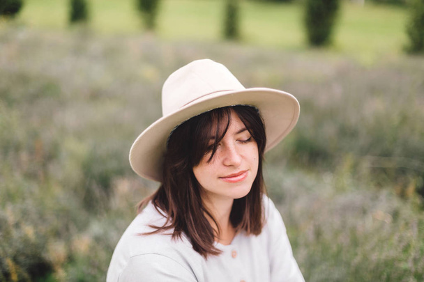 Stylish hipster girl in linen dress and hat sitting on bench at  - Foto, Bild