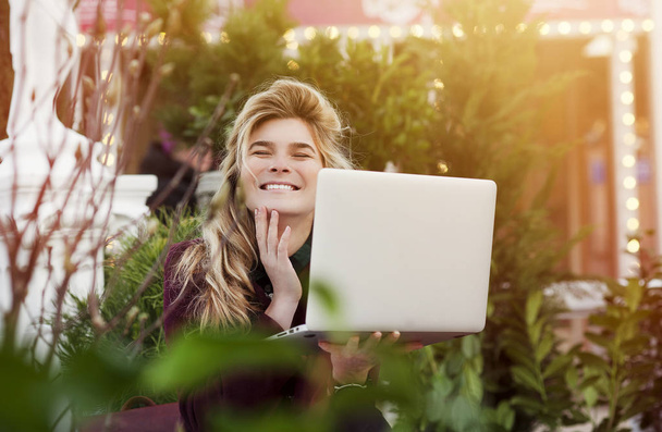 szép lány ül egy padon egy laptop a kezében egy új utcán a város. A koncepció munka öröm, szabadúszó és egy diák egy számítógépes - Fotó, kép