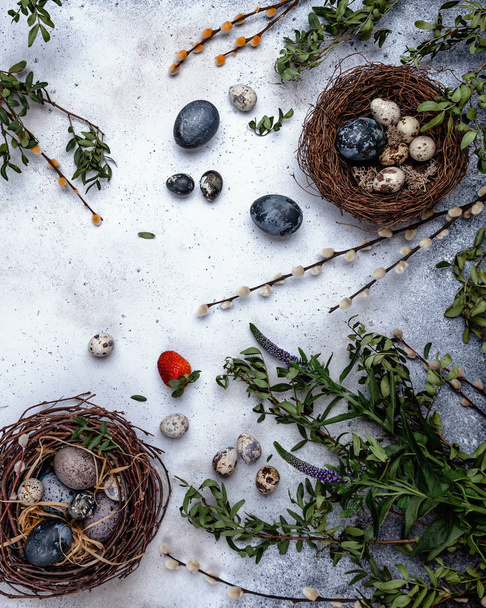 Top view of easter composition with eggs in nest, red strawberry and green branches on stone background  - Valokuva, kuva
