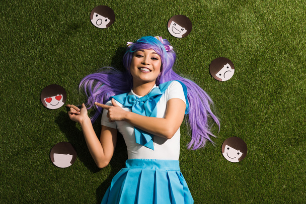 Asian anime girl in purple wig with emoticons lying on grass - Photo, Image
