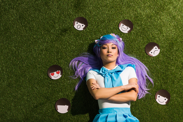 Asiatico anime ragazza in viola parrucca con emoticon sdraiato su erba
 - Foto, immagini