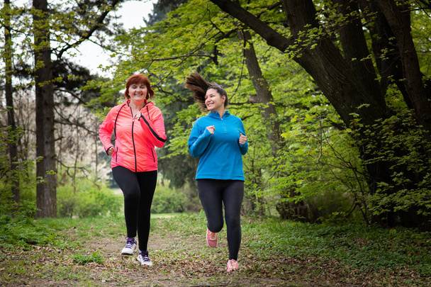 Matka a dcera nosí sportovní oblečení a běží v lese - Fotografie, Obrázek