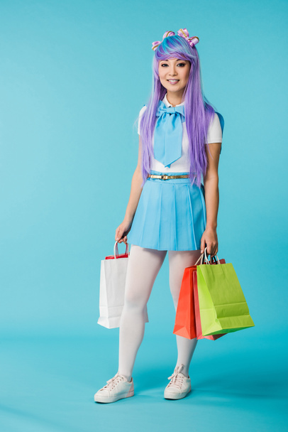 Full length view of asian anime girl holding shopping bags on blue - Фото, зображення