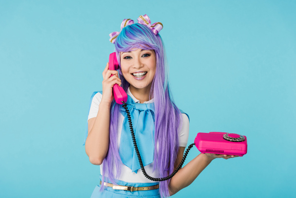 Smiling asian anime girl talking on telephone isolated on blue - Foto, Imagem