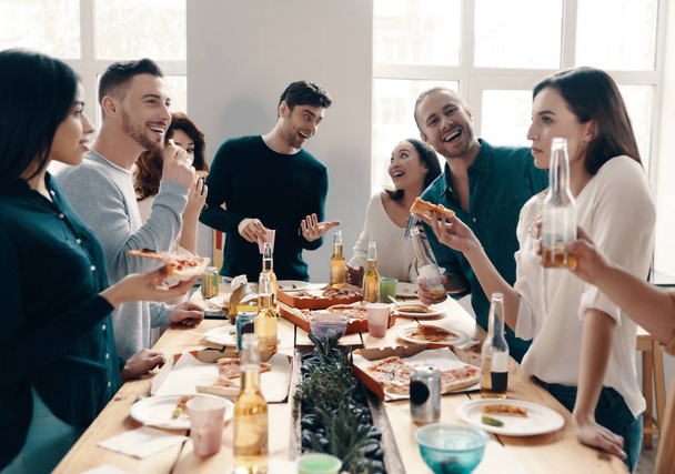 Great party. Group of young people in casual wear eating pizza and smiling while having a dinner party indoors - Photo, image