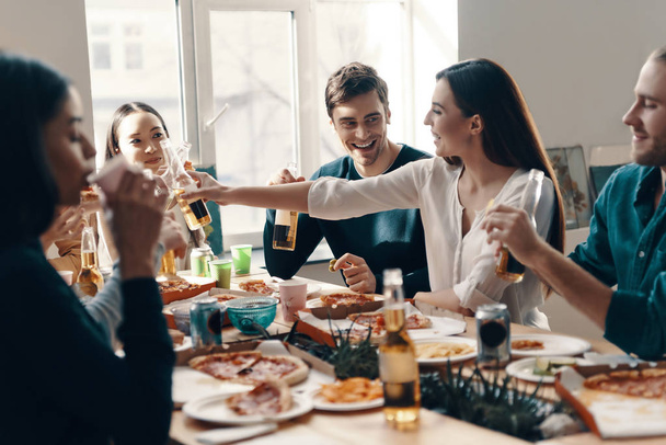 Having fun. Group of young people in casual wear eating pizza and smiling while having a dinner party indoors - Foto, imagen