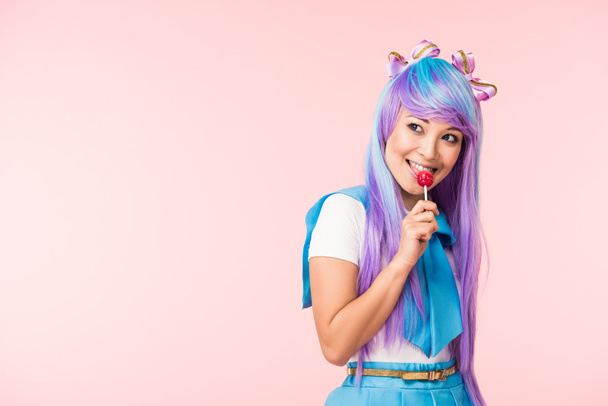 Happy asian otaku girl in wig eating lollipop isolated on pink - Φωτογραφία, εικόνα