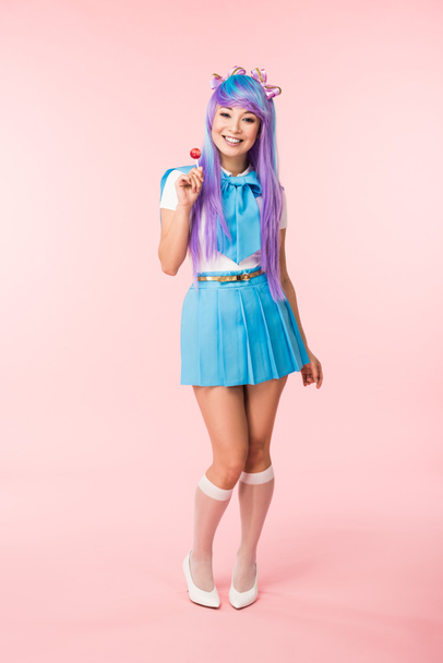 Full length view of smiling asian otaku girl holding lollipop on pink - Foto, Imagen