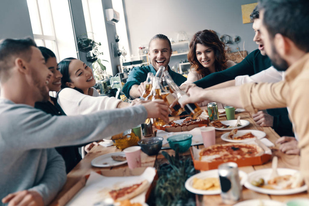 Quality time among friends. Group of young people in casual wear toasting each other and smiling while having a dinner party indoors        - Фото, зображення