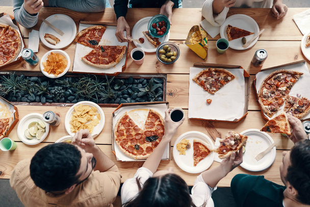 Любимая еда. Закрыть вид сверху на молодых людей, которые едят пиццу во время званого ужина в помещении
 - Фото, изображение