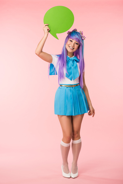 Full length view of smiling asian anime girl holding green speech bubble on pink - Photo, Image