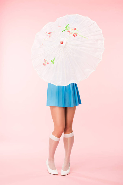 Full length view of girl in white knee socks holding paper umbrella on pink - Zdjęcie, obraz