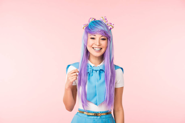 Gelukkig Aziatische anime meisje in paarse pruik glimlachend op roze - Foto, afbeelding