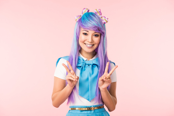 Joyful asian anime girl in purple wig showing peace signs isolated on pink - Photo, Image