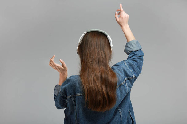 Mujer joven con auriculares escuchando música sobre fondo gris
 - Foto, imagen