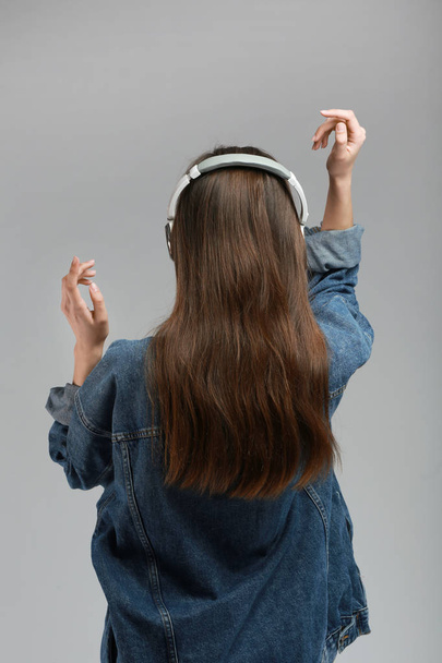 Mujer joven con auriculares escuchando música sobre fondo gris
 - Foto, imagen