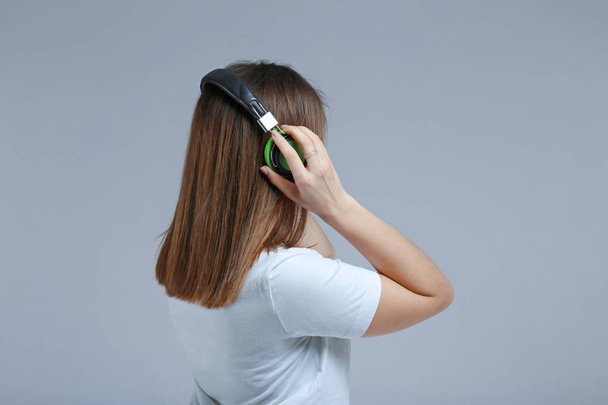Молода жінка з навушниками слухає музику на сірому фоні
 - Фото, зображення