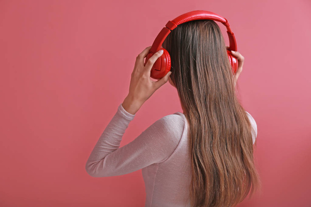 Young woman with headphones listening to music on color background - Photo, Image