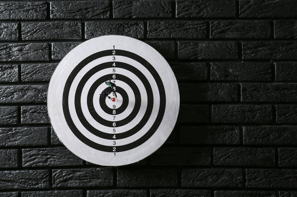 Dartboard with hit bullseye on dark brick wall - Фото, изображение