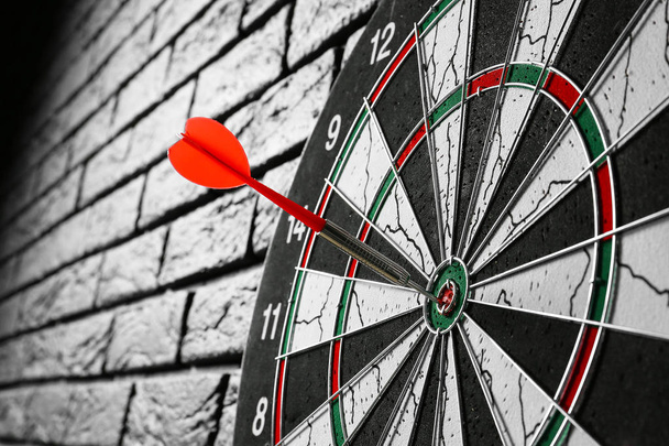 Dartboard with hit bullseye on dark brick wall, closeup - Photo, Image