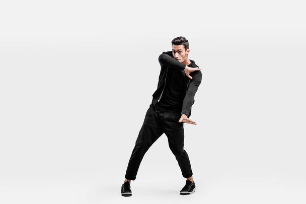 Dark-haired stylish man dressed in a stylish black clothes is dancing street dance. He makes stylized movements with his hands - Fotoğraf, Görsel